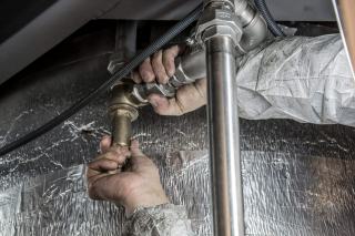 Plombier resserrant un raccord de canalisation au plafond après un dégât des eaux